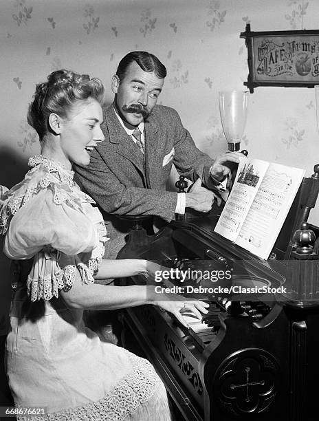 1900s SINGING COUPLE IN 19TH CENTURY DRESS WOMAN PLAYING PARLOR ORGAN MAN WITH HANDLEBAR MUSTACHE TURNING PAGES OF SHEET MUSIC