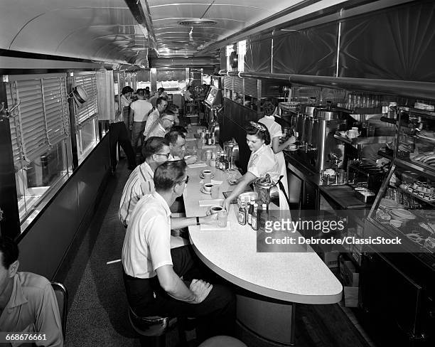 1950s 1960s INTERIOR OF A DINER WITH CUSTOMERS SEATED AT COUNTER AND WAITRESSES SERVING THEM