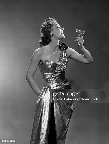 1950s WOMAN WEARING METALLIC EVENING GOWN HOLDING UP WINE GLASS PROFILE