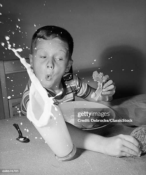 1960s BOY HAVING LUNCH KNOCKING OVER MILK REACHING FOR COOKIE SURPRISE SPLASH INDOOR