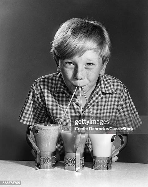 1950s 1960s PORTRAIT OF BLONDE BOY DRINKING WITH STRAWS FROM 3 MILKSHAKES SODAS SMILING LOOKING AT CAMERA