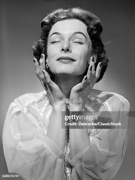 1950s WOMAN WEARING PEIGNOIR WITH EYES CLOSED HANDS HELD NEAR FACE ECSTATIC FACIAL EXPRESSION