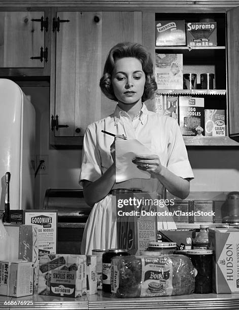 1960s WOMAN HOUSEWIFE IN KITCHEN CHECKING GROCERY FOOD SHOPPING LIST