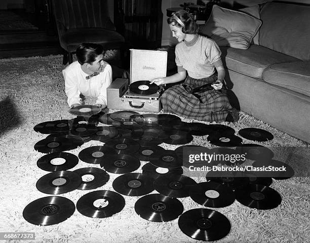 1950s TEENAGE COUPLE PLAYING MANY MUSIC RECORDS SPREAD OUT ON LIVING ROOM FLOOR