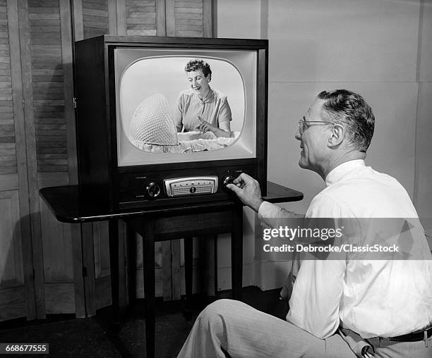 1950s MAN TUNING TELEVISION TO A PICTURE OF WOMAN LOOKING INTO BABY BASSINET