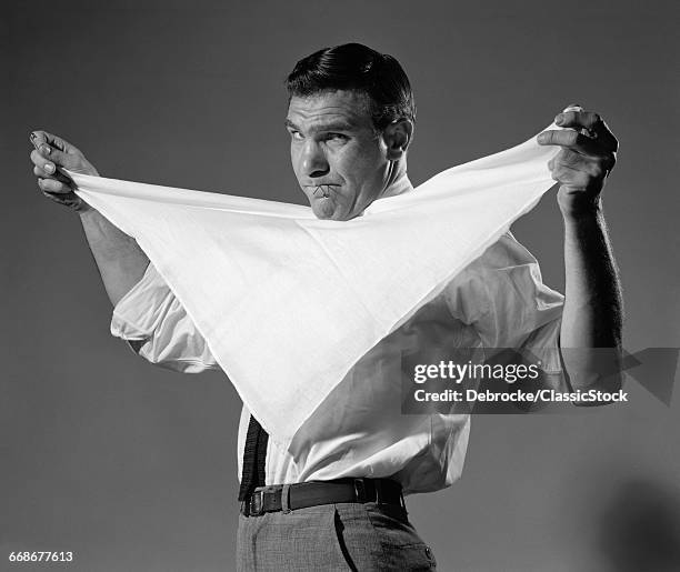 1950s 1960s MAN HOLDING CLOTH DIAPER FOLDED IN TRIANGLE UNDER CHIN WITH SAFETY PINS IN MOUTH LOOKING AT CAMERA