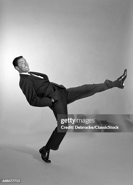 1960s SMILING BUSINESSMAN MAN WEARING A SUIT DOING A EXAGGERATED WALK WITH HANDS IN HIS POCKET KICKING LEG IN AIR