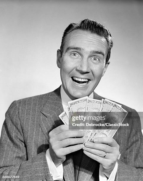 1950s HAPPY MAN WITH EXAGGERATED SMILE HOLDING FAN OF MONEY LOOKING AT CAMERA