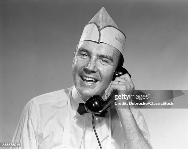 1950s MAN IN FOOD SERVICE UNIFORM TALKING ON TELEPHONE LOOKING AT CAMERA