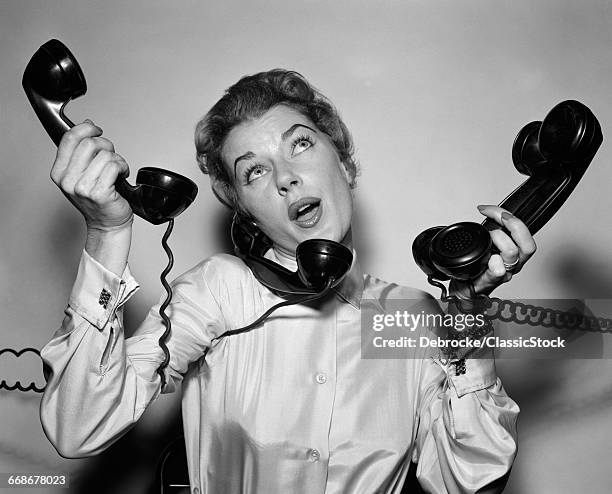 1950s HARRIED WOMAN HOLDING FOUR TELEPHONES TALKING ON ONE