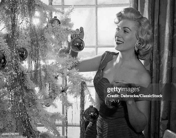 1950s WOMAN DECORATING CHRISTMAS TREE WITH FESTIVE GLASS BALLS