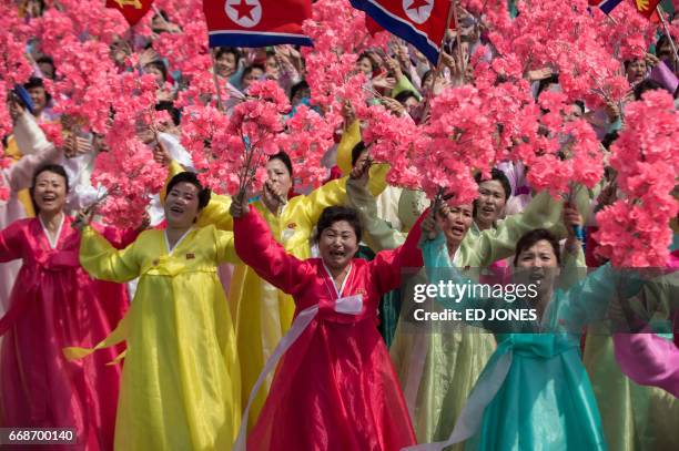 Women wearing traditional Korean dress wave flowers and shout slogans as they pass North Korea's leader Kim Jong-Un during a mass rally marking the...