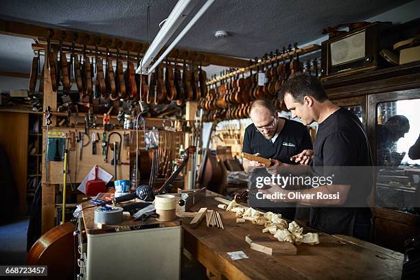 two luthiers in workshop working on violin - instrumentenmaker stockfoto's en -beelden