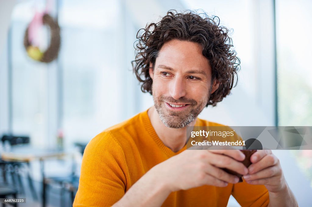 Portrait of smiling man with curly brown hair holding cup of coffee
