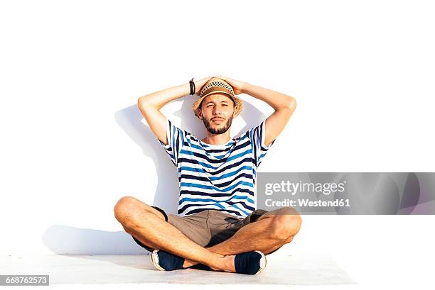 vacationer with straw hat and striped t-shirt sitting on spur leaning against white wall - striped shorts stock pictures, royalty-free photos & images