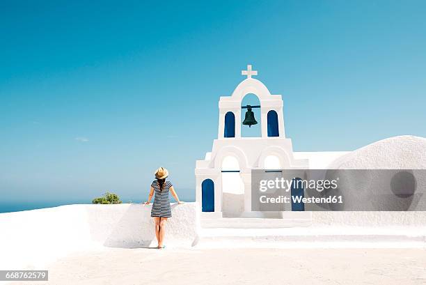 greece, santorini, oia, back view of woman standing next to bell tower looking to the sea - santorini stockfoto's en -beelden