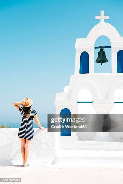 greece, santorini, oia, back view of woman standing next to bell tower looking to the sea - mediterranean-blue-roof-santorini stock pictures, royalty-free photos & images