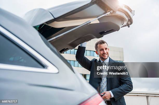 smiling businessman at car boot - auto stehend stock-fotos und bilder