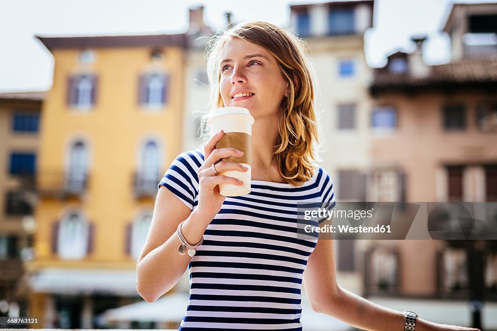 Italy, Udine, portrait of smiling young woman with coffee to go