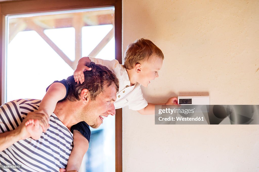 Father carrying son on shoulders, adjusting thermostat