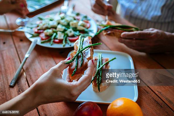 woman's hand holding bread slice with cured ham and grilled green asparagus - white plate stock pictures, royalty-free photos & images