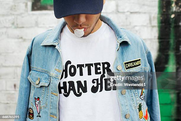 young man with gum bubble wearing t-shirt with saying 'hotter than hell' - jeansjacke stock-fotos und bilder