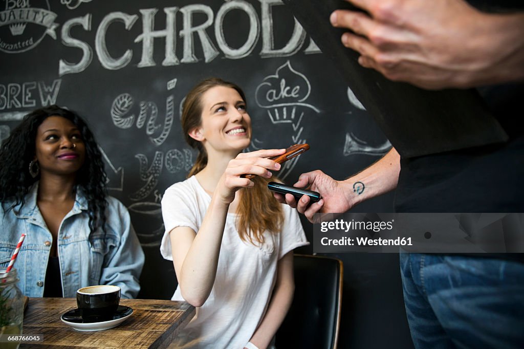 Friends in cafe paying with smartphone