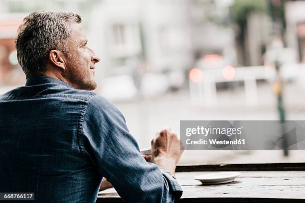 mature man sitting in cafe looking out of window - solo un uomo maturo foto e immagini stock