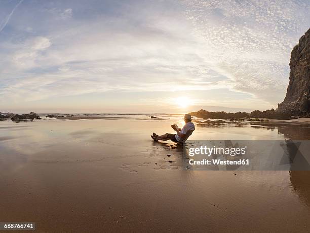 portugal, senior man sitting at beach, reading book - homem costas - fotografias e filmes do acervo