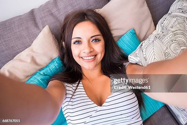 portrait of smiling teenage girl lying on the couch taking selfie with cell phone - lying on back girl on the sofa stock pictures, royalty-free photos & images