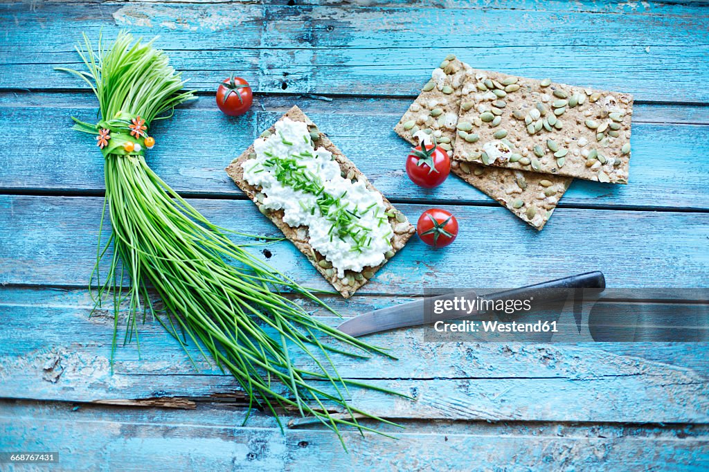 Crispbread, cream cheese, bunch of chive, cocktail tomatos and knife on turquoise wood