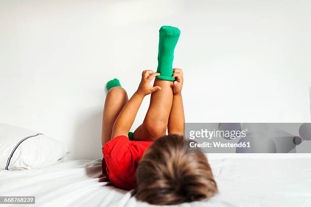back view of little boy lying on bed putting on his green socks - getting dressed stockfoto's en -beelden