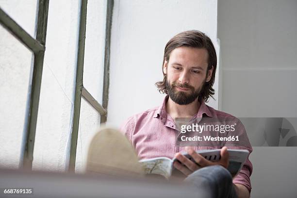 man sitting on window sill reading magazine - homens de idade mediana imagens e fotografias de stock