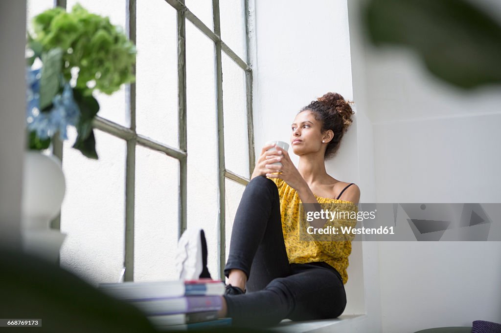 Young woman sitting on window sill with a cup of coffee