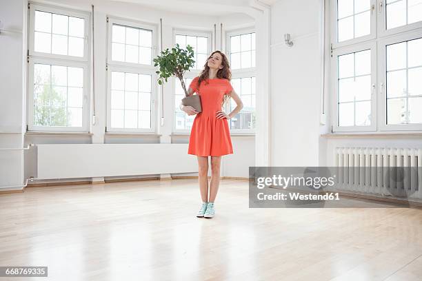 smiling woman holding plant in empty apartment - pot plant stock pictures, royalty-free photos & images