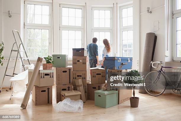 couple with cardboard boxes in new apartment looking out of window - paar gruppierung stock-fotos und bilder