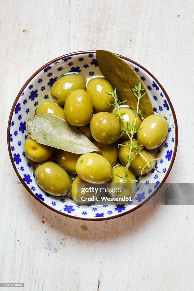 Green olives in bowl with thyme and bay leaf