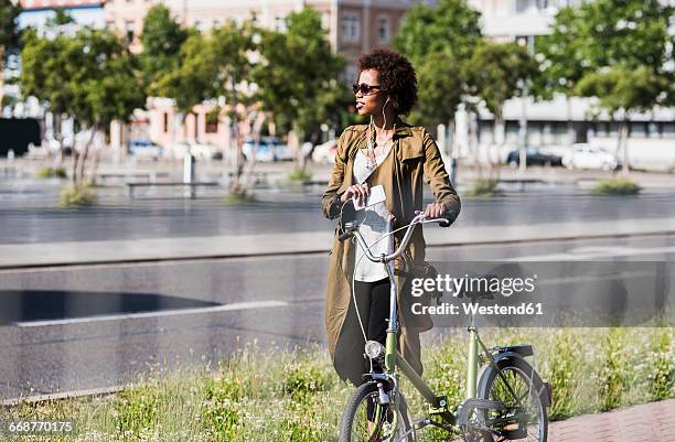 young woman with smartphone and earphones pushing bicycle - folding bike stockfoto's en -beelden