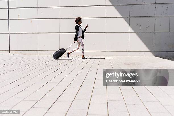 walking businesswoman with trolley bag looking at her smartphone - rollkoffer stock-fotos und bilder