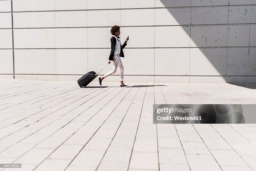 Walking businesswoman with trolley bag looking at her smartphone