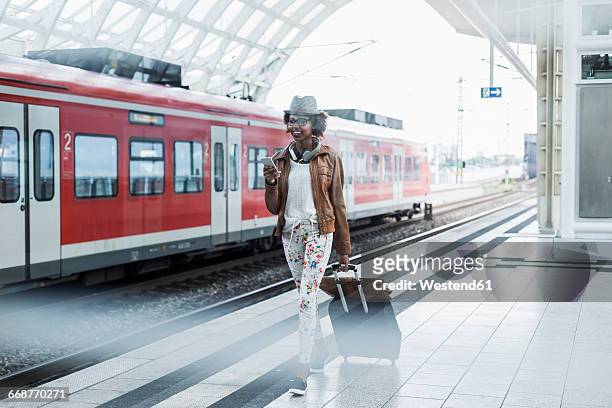 young woman with trolley bag and smartphone at platform - station stock-fotos und bilder