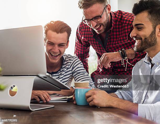 three happy young professionals sharing laptop in office - leisure work coffee happy stockfoto's en -beelden