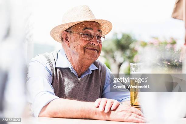 portrait of happy senior man drinking glass of beer in a sidewalk cafe - man sipping beer smiling stockfoto's en -beelden