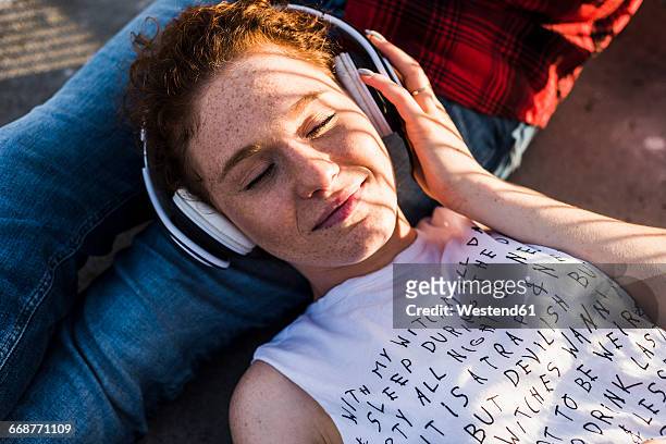 young woman with headphones lying on boyfriend's lap - listening stockfoto's en -beelden