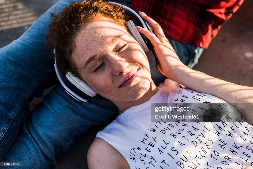 Young woman with headphones lying on boyfriend's lap
