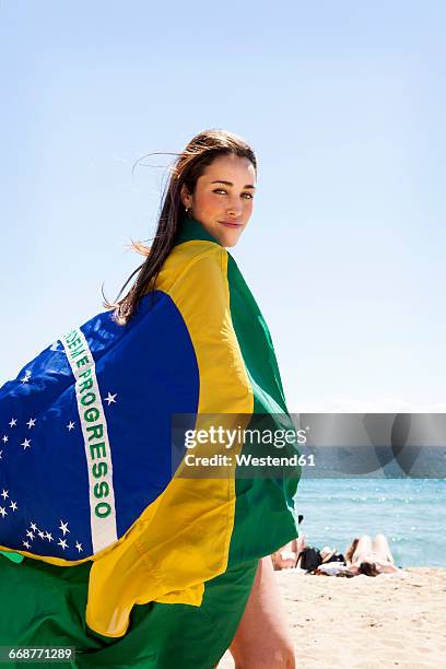 young brunette woman playing with brazilian flag at the beach - beauty fan event stock-fotos und bilder