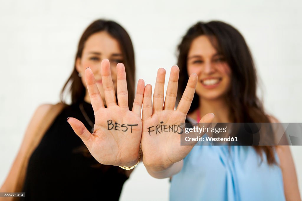 Two young women showing their palms with writing 'best friends'