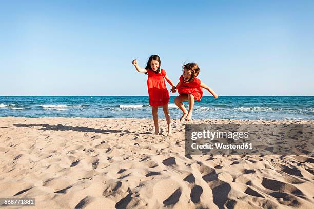 two little sisters jumping together on the beach - red dress child stock pictures, royalty-free photos & images