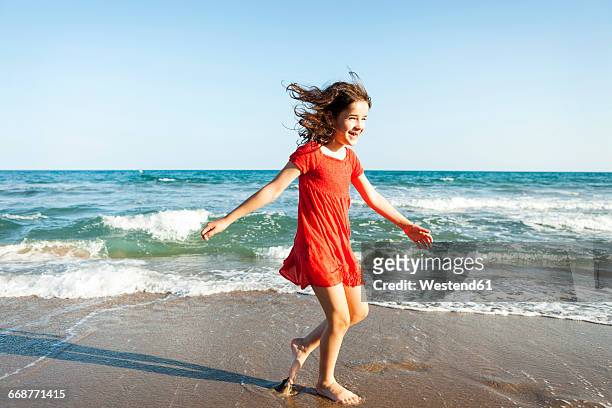 happy little sisters walking at waterside of the beach - red dress child stock-fotos und bilder