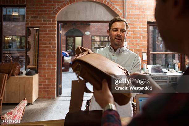 man handing over leather bag in shop - leather bag stock pictures, royalty-free photos & images
